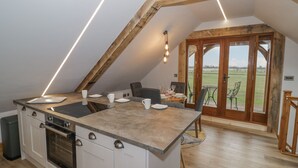 A kitchen with a central island, wooden beams, and a dining area with a view. - Hallgarth Farm Holiday Lodge (Pershore)