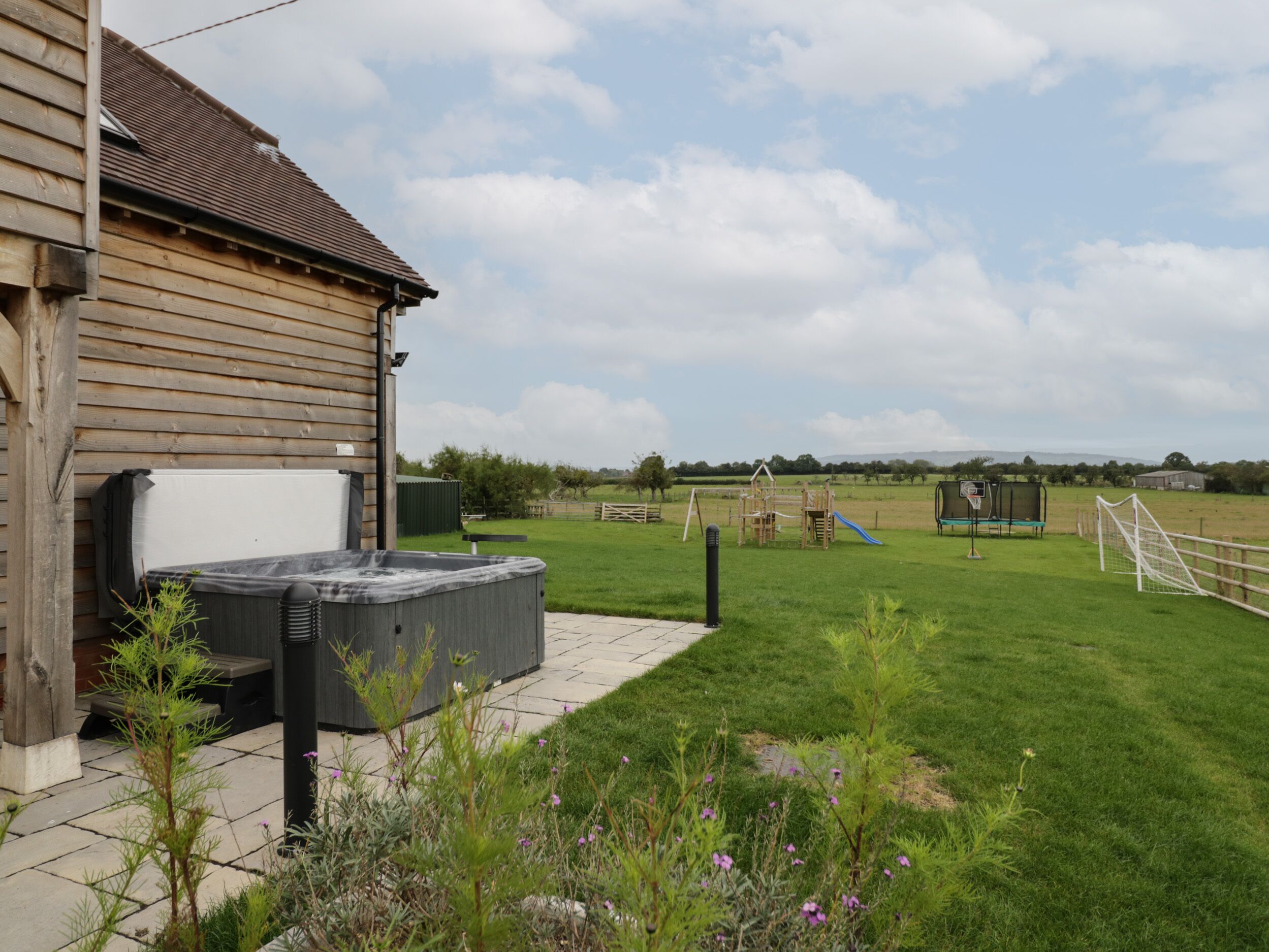 A wooden building with a hot tub and a grassy area with playground equipment.