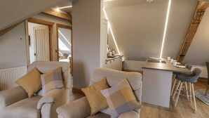 A modern loft bedroom with a sloped ceiling, a dining area with a bar, and a cozy seating area with armchairs. - Hallgarth Farm Holiday Lodge (Pershore)