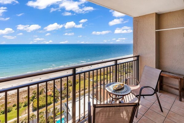 Un balcon avec vue sur l’océan, une table avec des chaises et une petite table agrémentée d’un objet décoratif.
