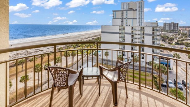 A balcony with a view of the beach and ocean, featuring two chairs and a small table.