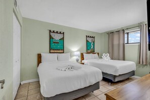 Une chambre d’hôtel avec deux lits, une table en bois et des œuvres d’art accrochées aux murs.