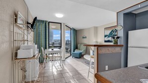 A compact kitchen with a dining area, a small table, and a view of the city through a large window.