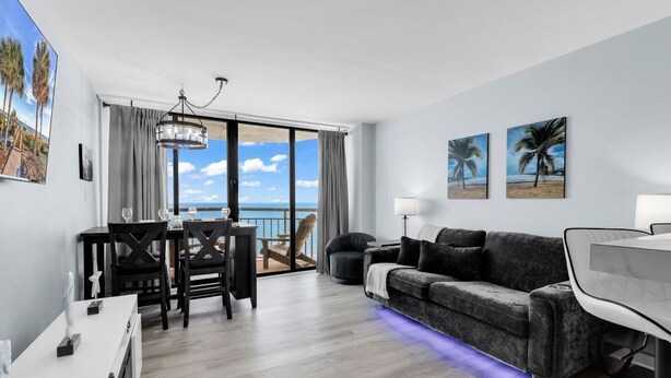 Un soggiorno moderno con divano, tavolo da pranzo e sedie, un balcone vista mare e opere d'arte alle pareti.