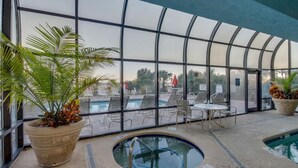 Area piscina interna con pareti in vetro trasparente, poltrone relax e vasca idromassaggio.