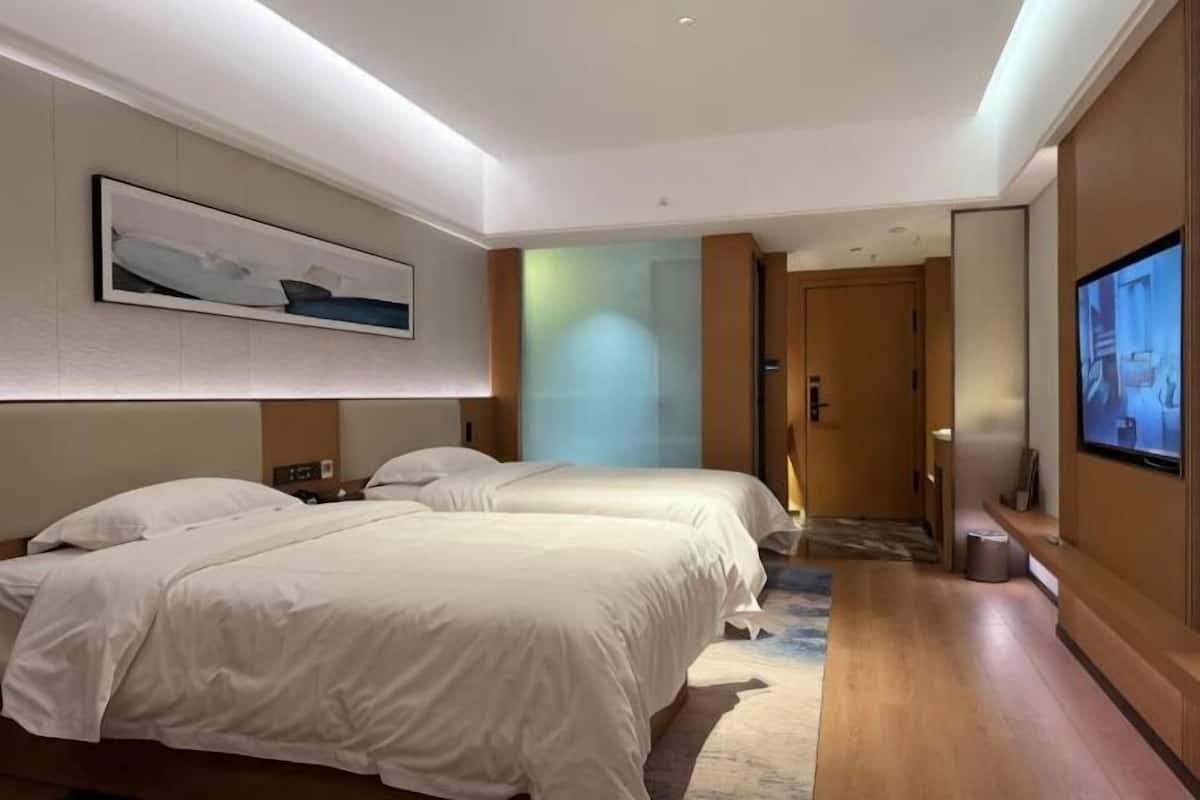 A hotel room with two beds, a flat-screen TV, a painting on the wall, and a wooden floor.