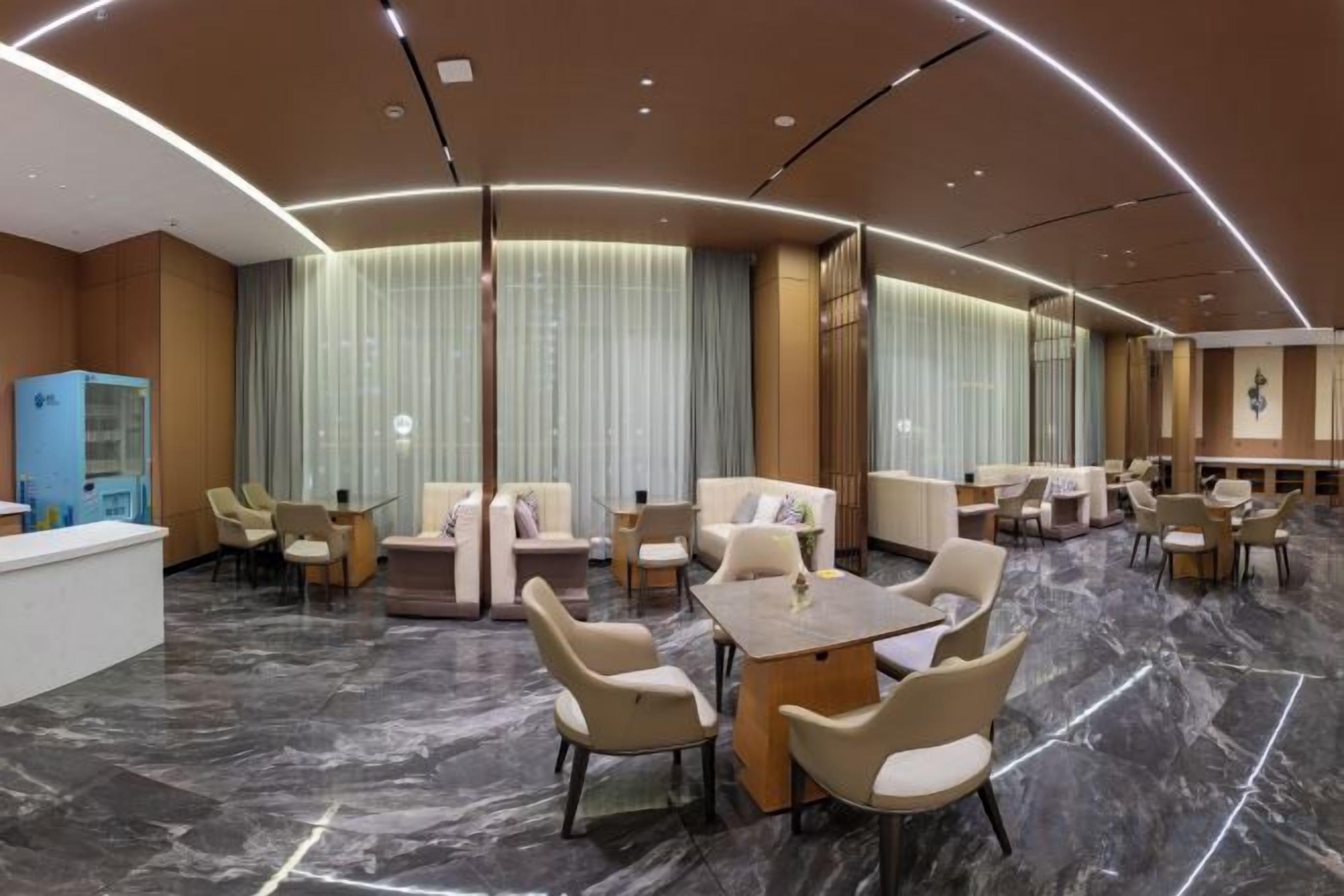 Rebedor d'hotel amb taulell de recepció, zones d'estar i una finestra gran amb cortines.