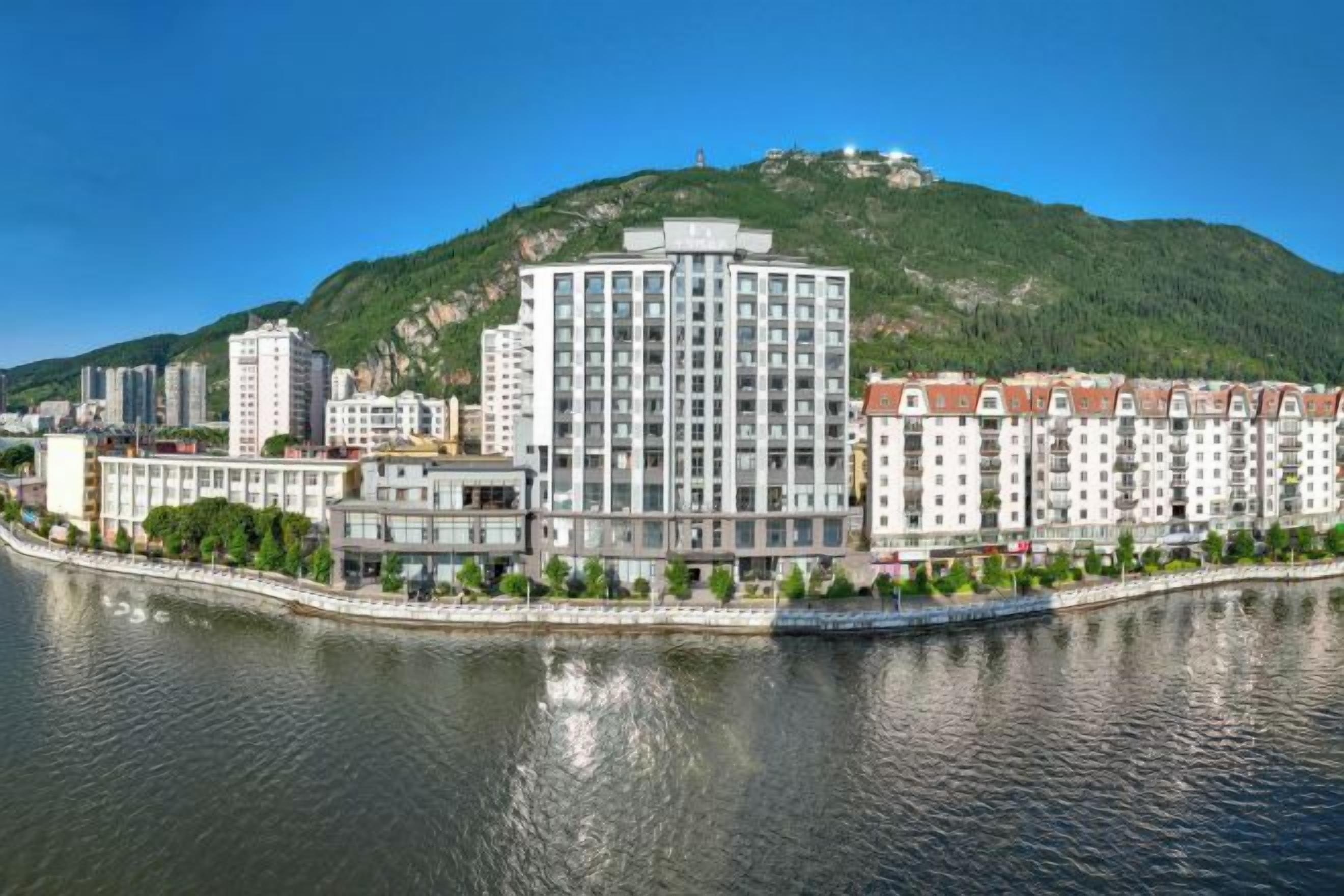 A hotel with a modern design, situated by a river, with a view of a hill in the background.