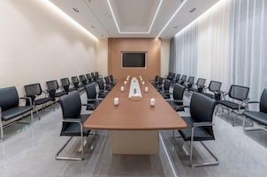 A conference room with a long table, chairs, and a screen.