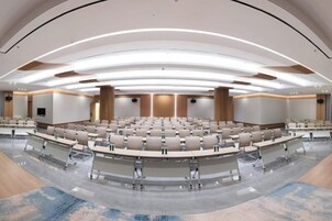 A large conference room with a curved layout, multiple tables, and a central stage.
