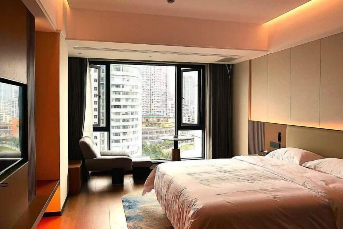 A modern hotel room with a large bed, a seating area, and a view of high-rise buildings.