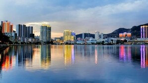 A city skyline with high-rise buildings reflected in calm water. - Shihaolou Hotel (Gejiu)