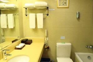 Un baño con un lavabo amarillo, un espejo, un inodoro y una bañera. Hay toallas colgadas en un perchero y un cuadro en la pared.