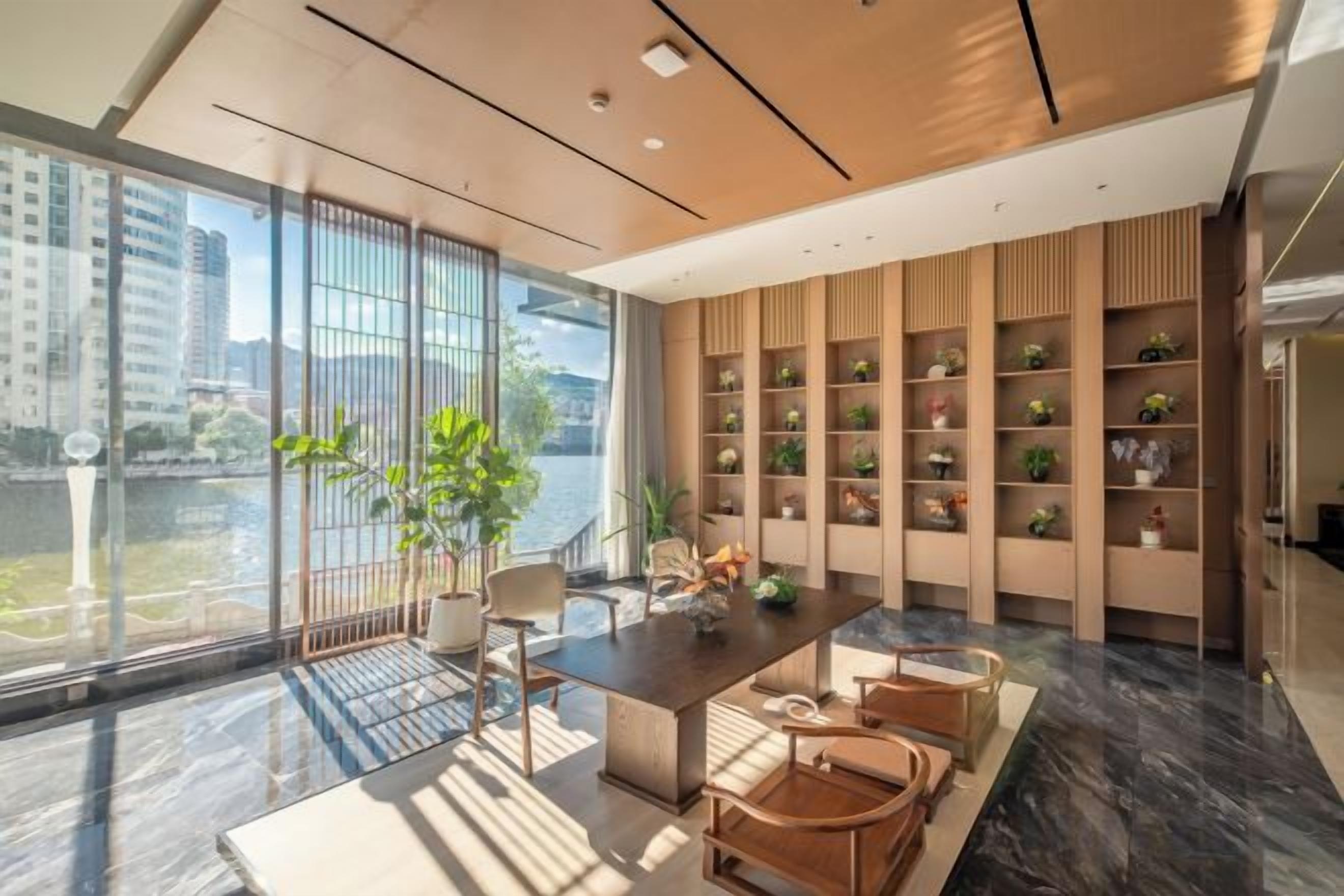 Un interior moderno con comedor, ventanas amplias y estanterías empotradas con plantas.