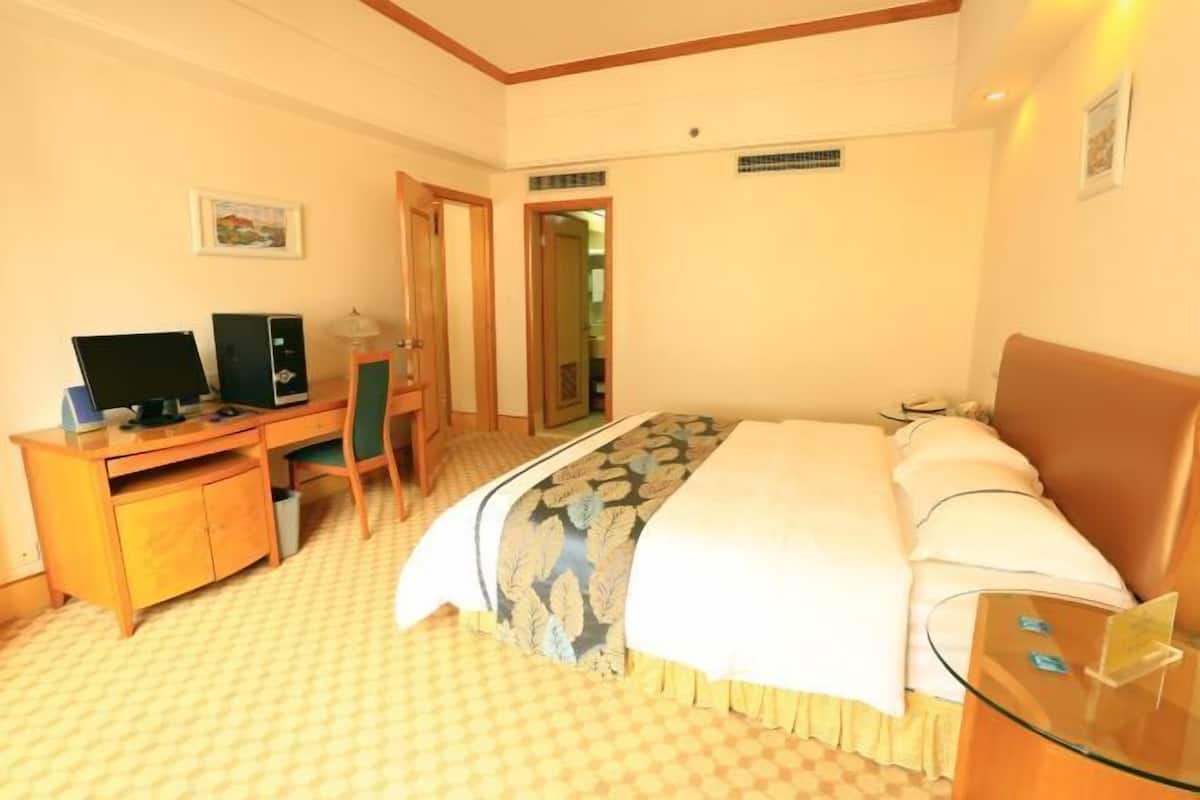 A hotel room with a bed, a desk with a computer, a chair, and a glass table.