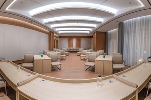 Un salón de conferencias con disposición en curva, varias mesas y sillas.