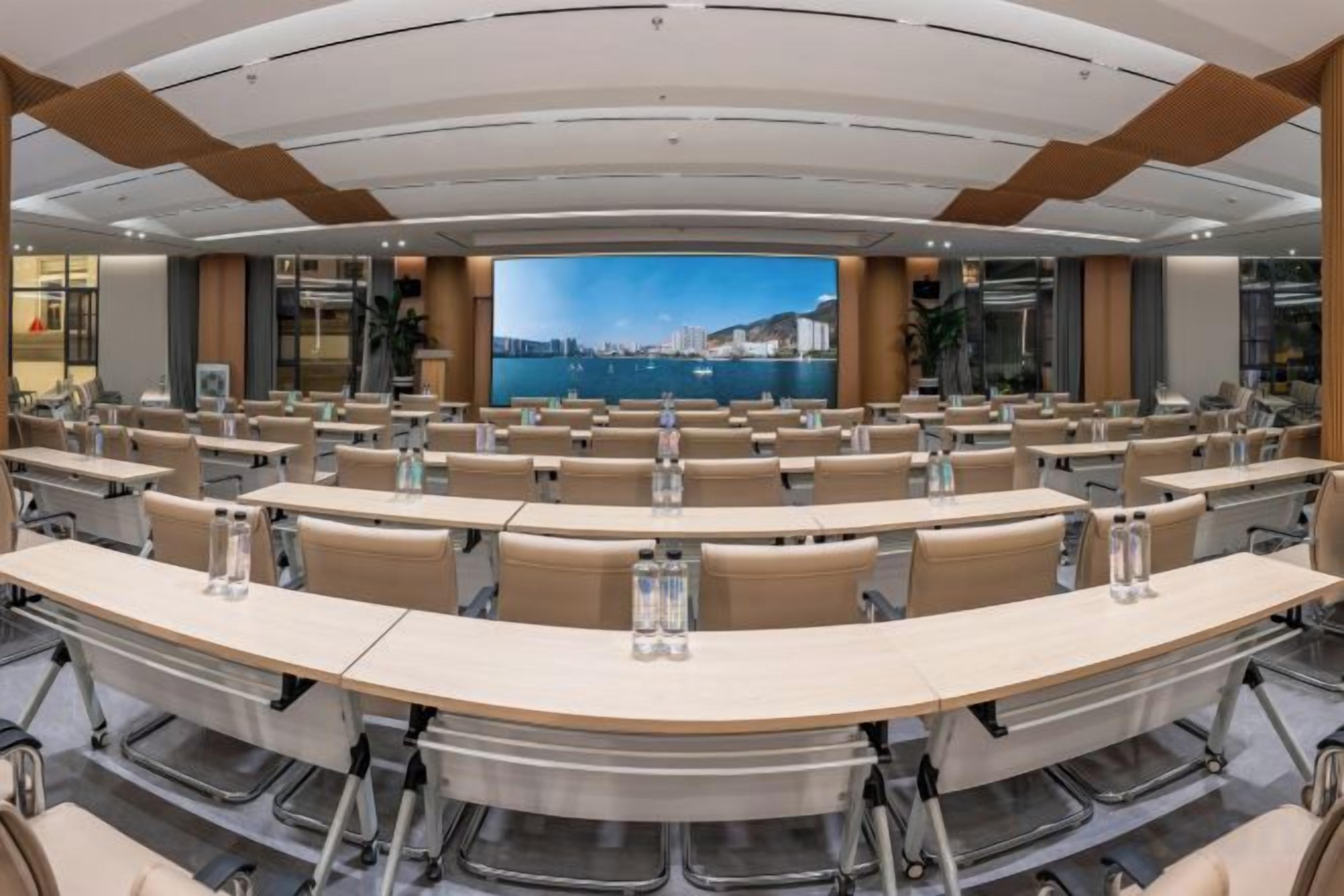 Una sala de conferències amb una pantalla gran, diverses taules i cadires disposades per a presentacions.
