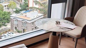 A balcony with a round marble table, a beige chair, and a view of buildings and trees. - Shihaolou Hotel (Gejiu)