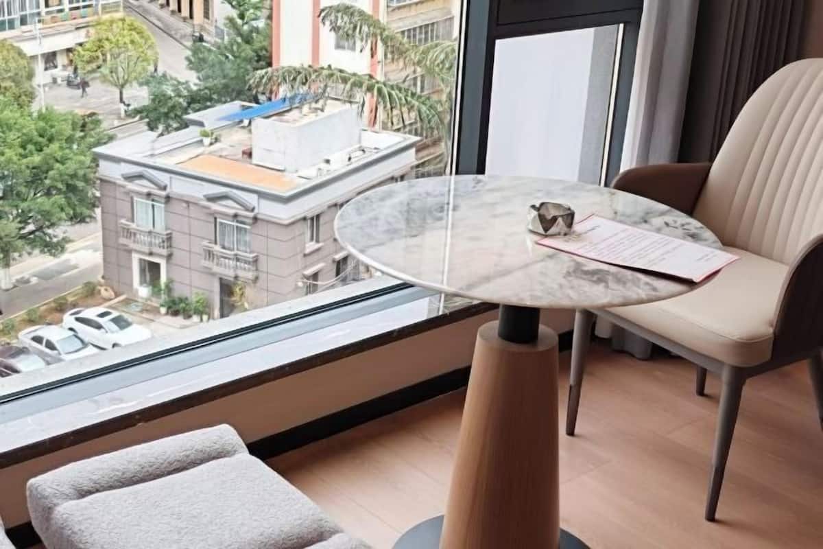 A balcony with a round marble table, a beige chair, and a view of buildings and trees.