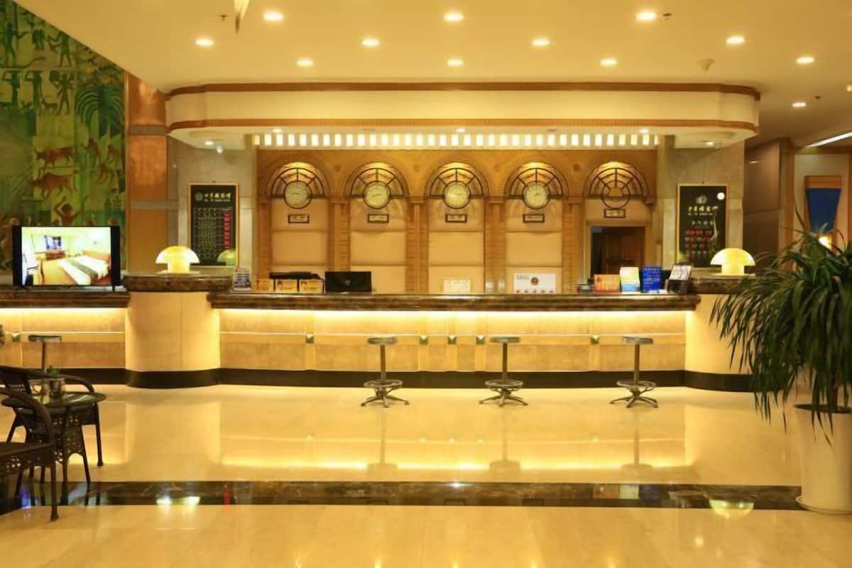 A hotel reception area with a marble counter, multiple clocks, and a television screen.