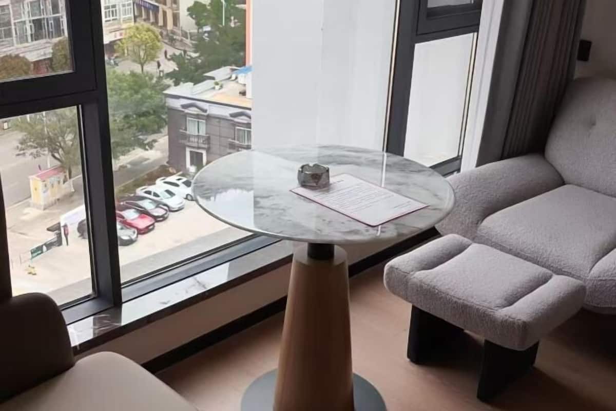 A modern hotel room with a glass table, a view of the street outside, and a grey sofa.