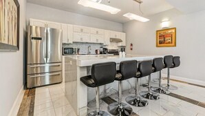 A modern kitchen with white cabinets, a stainless steel refrigerator, a central island with bar stools, and a microwave. - 20% OFF Monthly | 10% OFF Weekly-Breathtaking Condo with Excellent Amenities (New Orleans)
