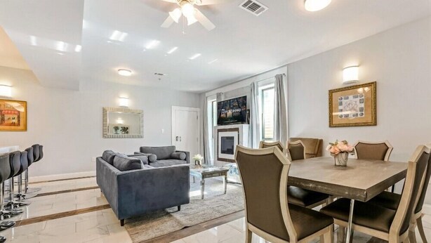 A modern living room with a grey sofa, a dining table with chairs, and a TV mounted above the fireplace. - 20% OFF Monthly | 10% OFF Weekly-Breathtaking Condo with Excellent Amenities (New Orleans)