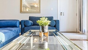 A modern living room with a blue sofa, a glass coffee table, and a potted plant. - 20% OFF Monthly | 10% OFF Weekly-Breathtaking Condo with Excellent Amenities (New Orleans)