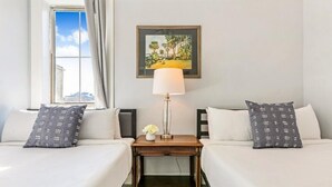 A hotel room with two beds, a nightstand with a lamp, a framed painting, and a window with curtains. - 20% OFF Monthly | 10% OFF Weekly-Breathtaking Condo with Excellent Amenities (New Orleans)
