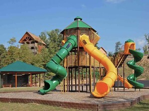 A playground with two slides and a wooden playhouse. - Fuzzy's Dollywood View⛰, Location, 4 KING beds (Sevierville)