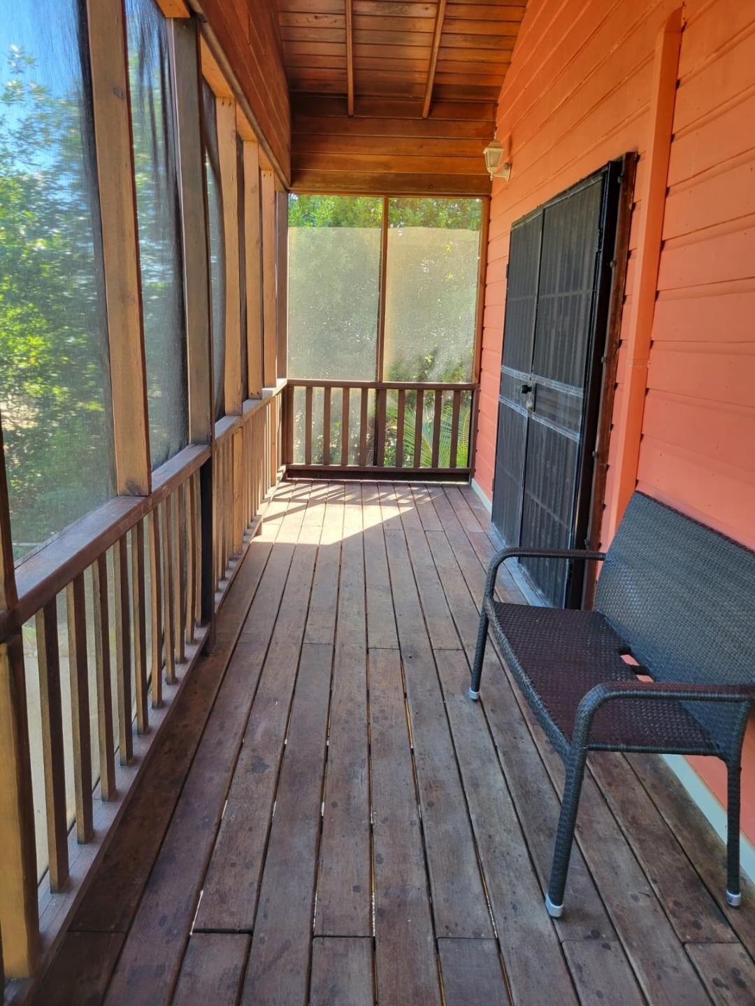 Une terrasse en bois avec un banc et une véranda grillagée.