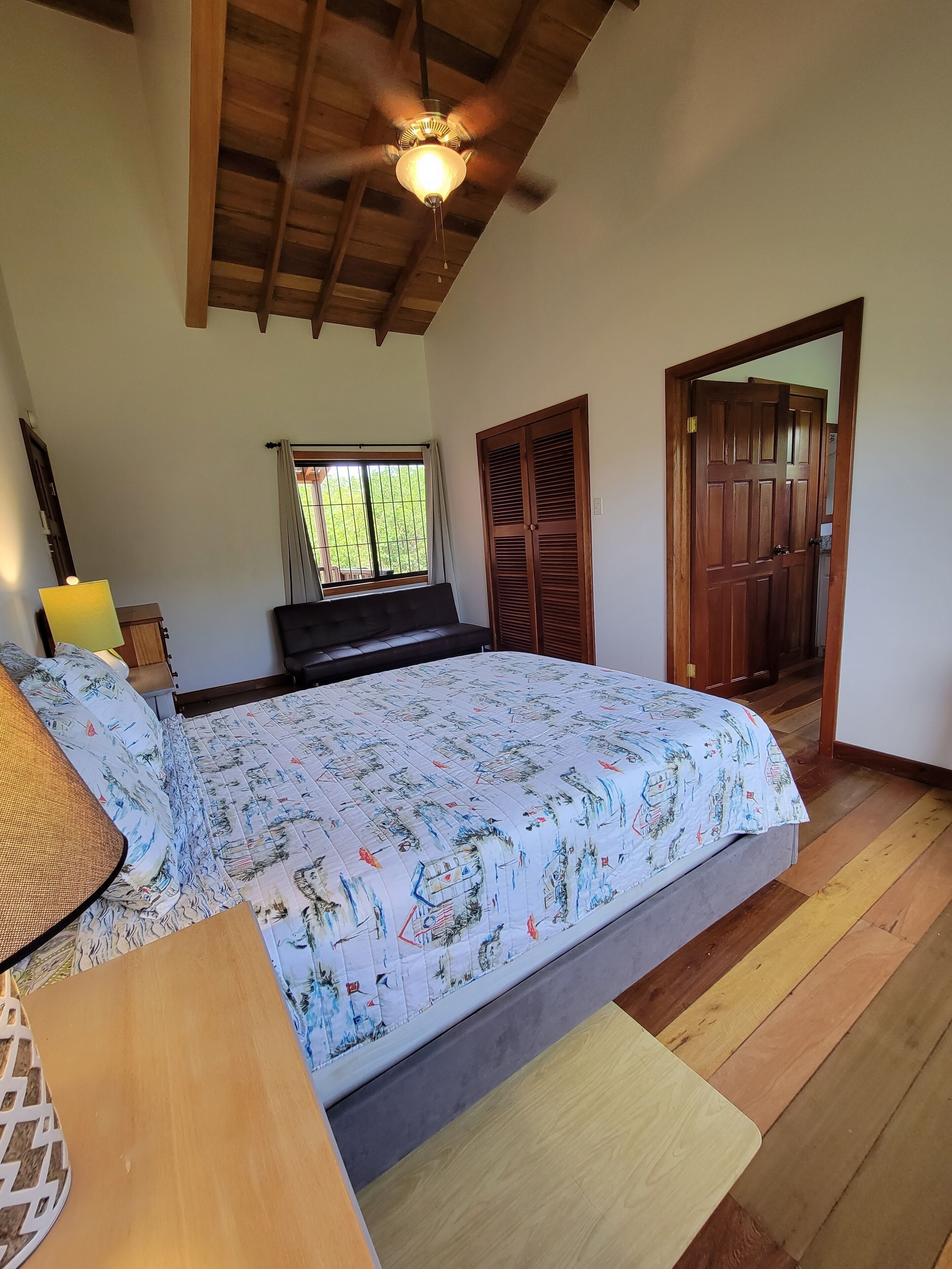 Um quarto com uma cama, um ventilador de teto, uma janela e uma porta.