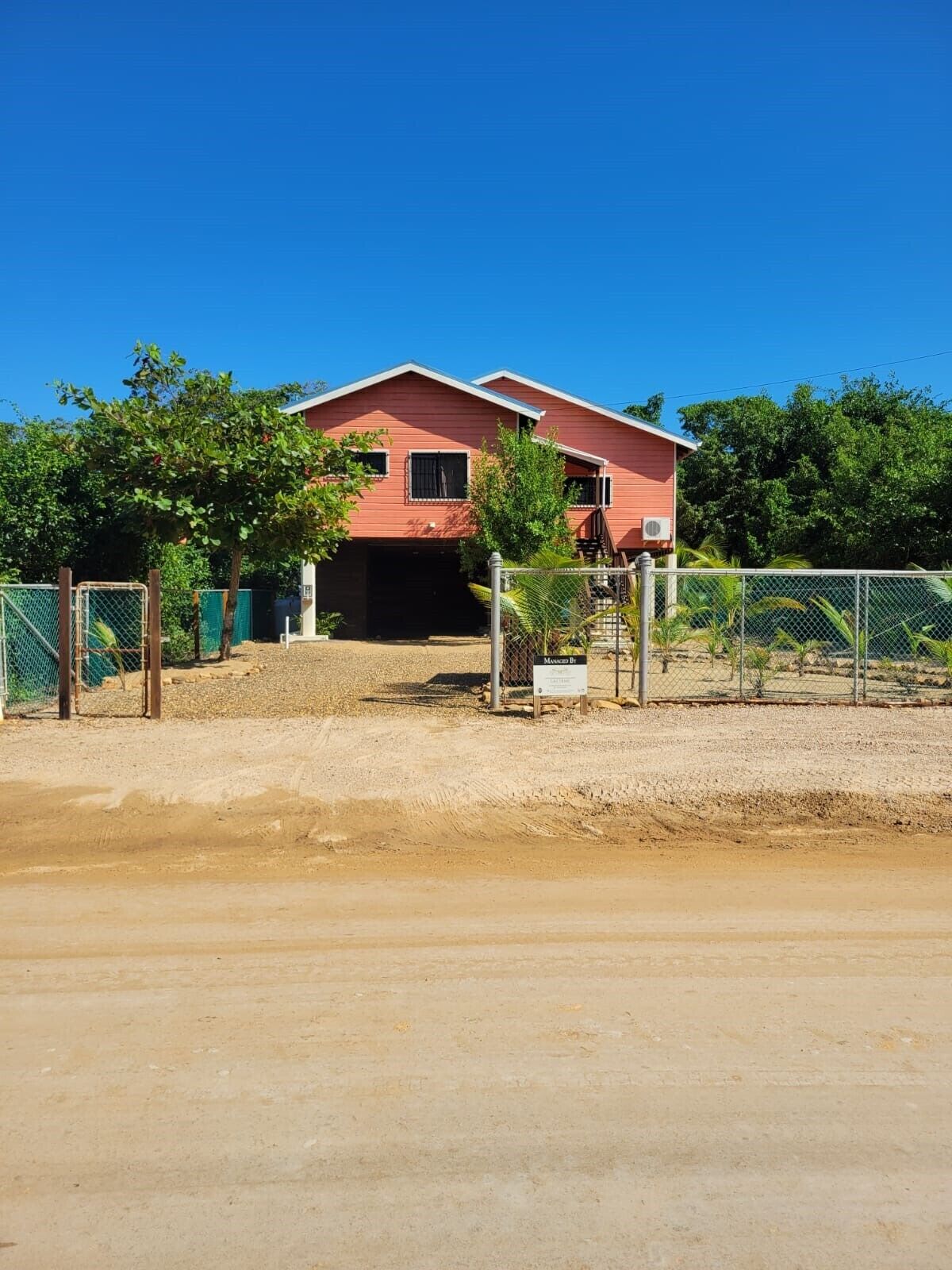 Una casa de dos pisos con fachada roja, un camino de entrada cubierto y un patio cercado.
