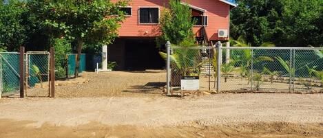 Una casa de dos pisos con fachada roja, un camino de entrada cubierto y un patio cercado.