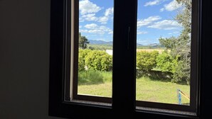 Una ventana con vista a un campo verde y árboles bajo un cielo despejado.