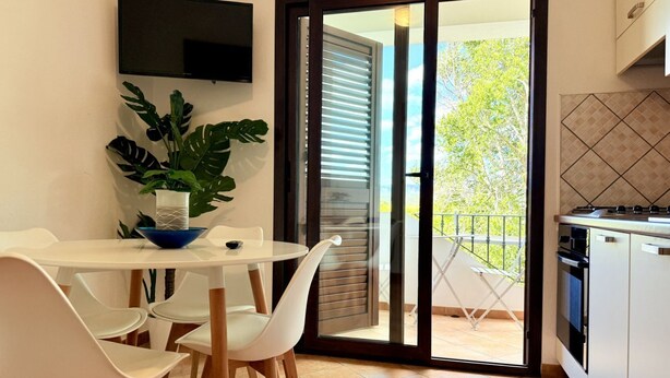 Una cocina moderna con comedor, televisor montado en la pared y puerta corrediza de vidrio que da a un balcón.
