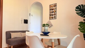 Un comedor con una mesa redonda, sillas blancas, un sofá gris y una planta sobre la mesa.