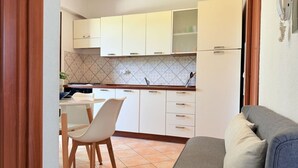 Una cocina compacta con armarios blancos, una mesa de comedor con sillas y un sofá gris en primer plano.