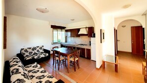 A living room with a sofa and a dining table, a kitchen with cabinets and a stove, and a hallway with a door. - [Panorama] View and Comfort a few steps away from the beach (Orosei)