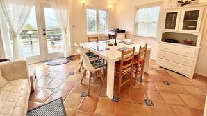 Een eetruimte met een tafel, stoelen en een kroonluchter. Er is ook een keuken met kastjes en een raam.