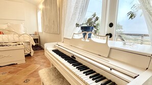 Een piano in een kamer met een bed, nachtkastje en een raam met gordijnen.