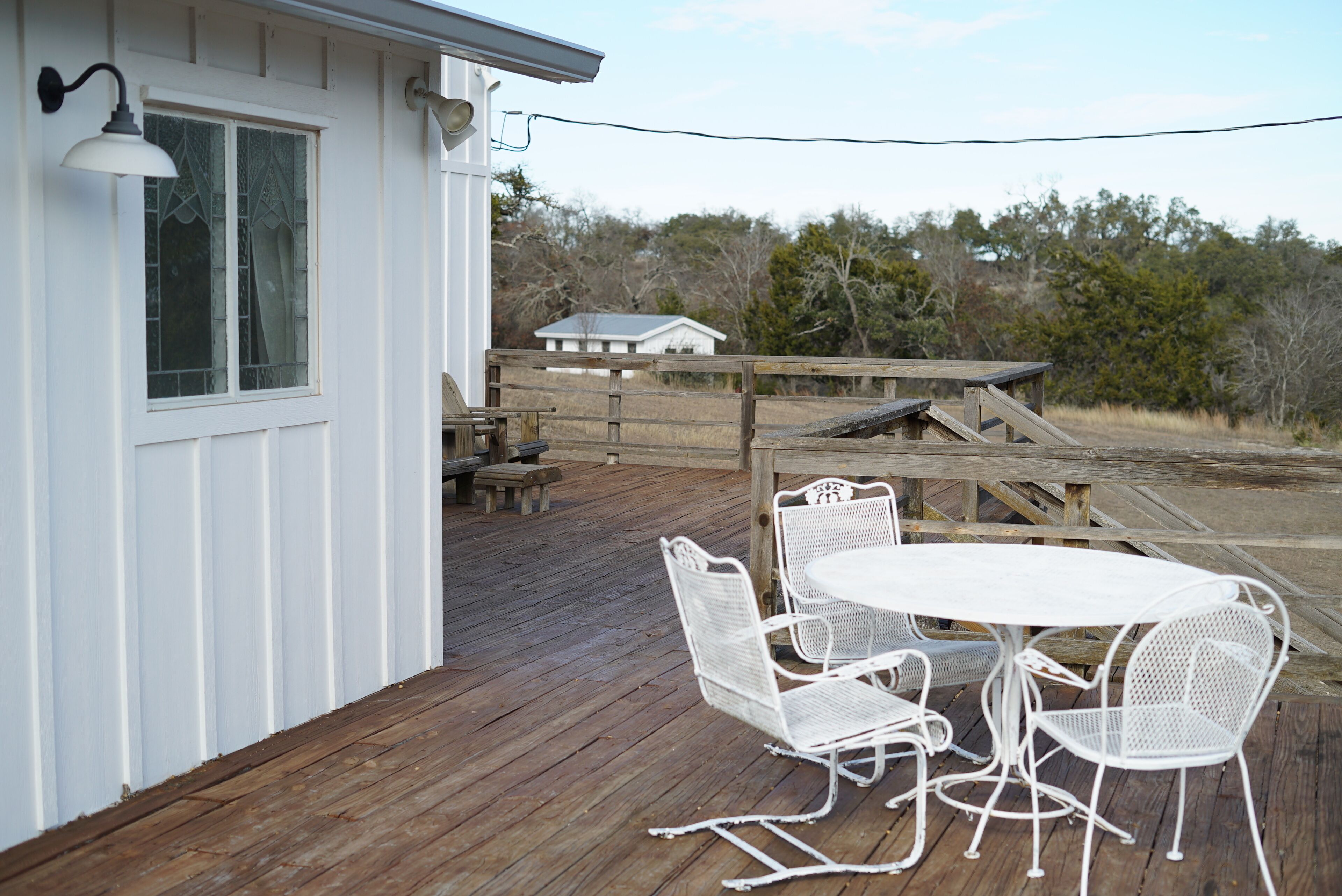 A wooden deck with a white table and chairs, a bench, and a railing.