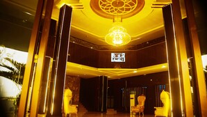 Un vaste hall d’entrée agrémenté d’un grand lustre, de fauteuils élégants et d’un écran de télévision fixé au mur.