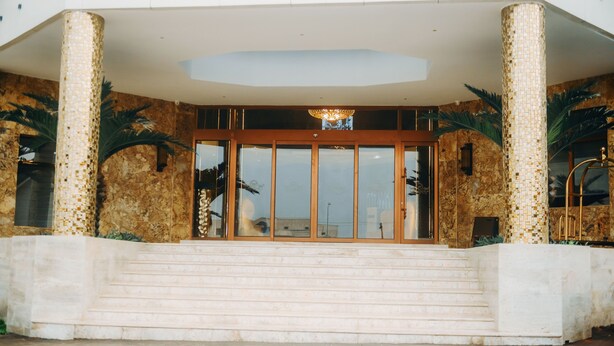 L’entrée d’un hôtel, avec un grand escalier, de larges colonnes et un lustre moderne.
