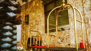 Un hall d’hôtel avec un mur en pierre, un extincteur rouge et un ascenseur doré.