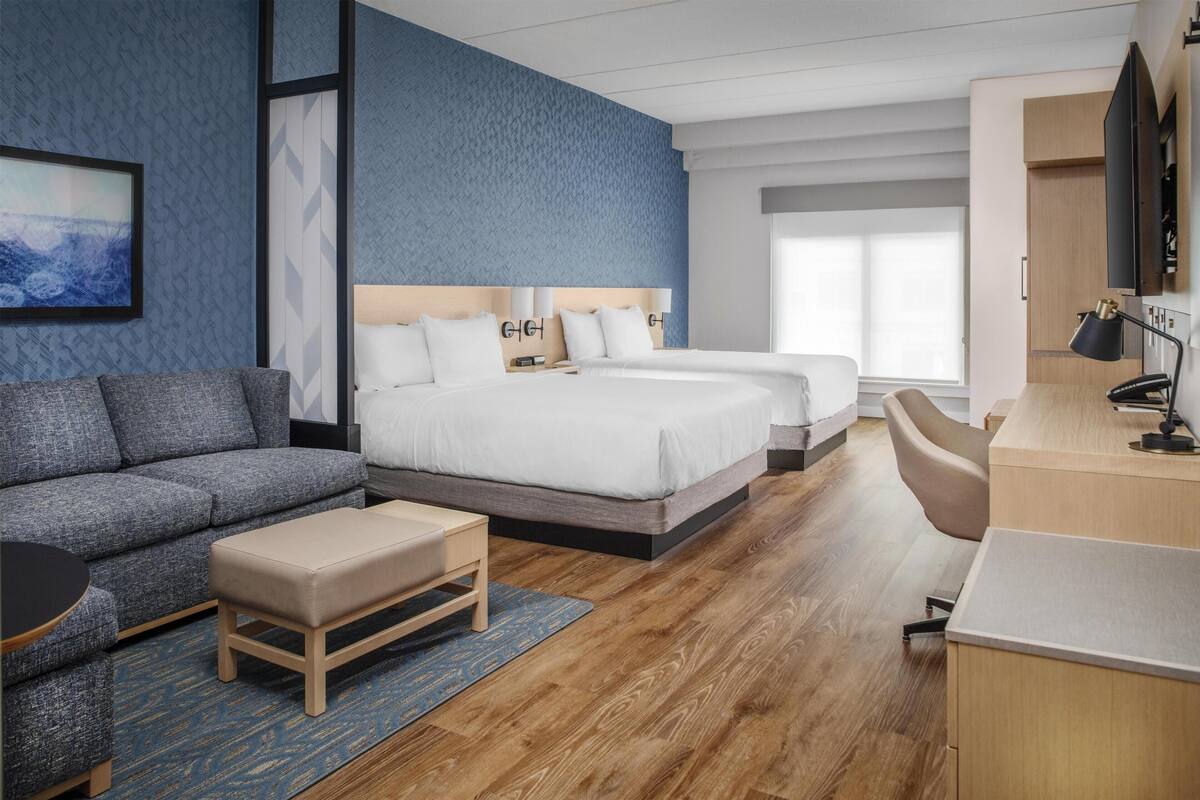 A modern hotel room with a large bed, a sofa, a desk, and a TV.