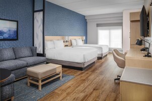 Quarto de hotel moderno com uma cama grande, um sofá, uma escrivaninha e uma televisão.