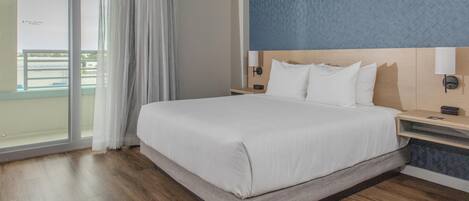 Une chambre d’hôtel avec un grand lit, une table de chevet, une lampe fixée au mur et une vue sur le balcon.