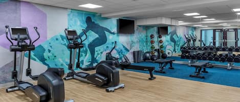 Un gimnasio con cintas de correr, elípticas y pesas libres.
