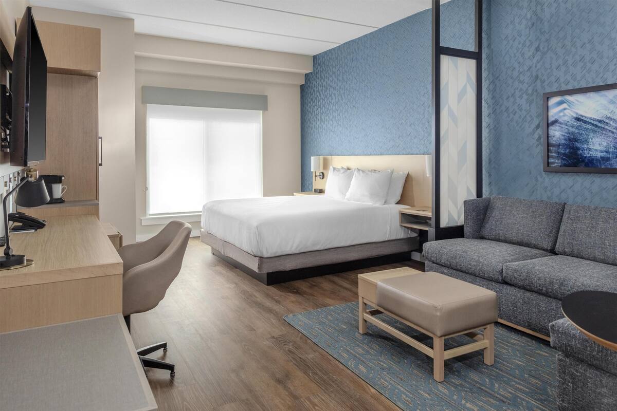 A modern hotel room with a bed, a desk, a sofa, and a TV.